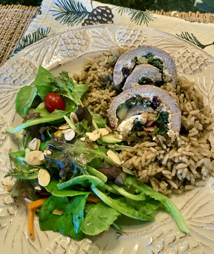 Two slices of apple stuffed pork tenderloin on a bed of wild rice next to a side salad.
